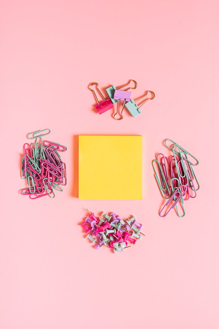 Vibrant flat lay of colorful office supplies on a pink surface.