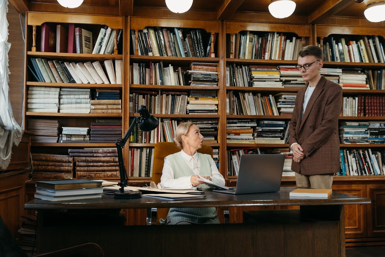 A man and woman engaged in a discussion in a university library with bookshelves.
