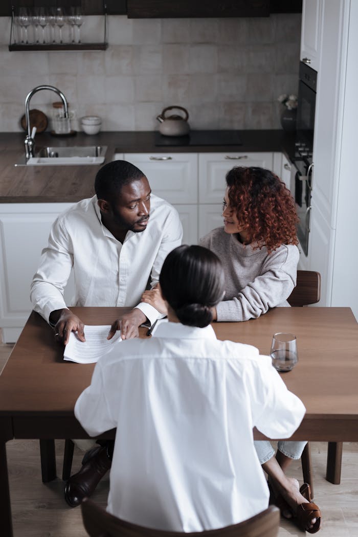Three adults discussing documents at a table in a modern kitchen.